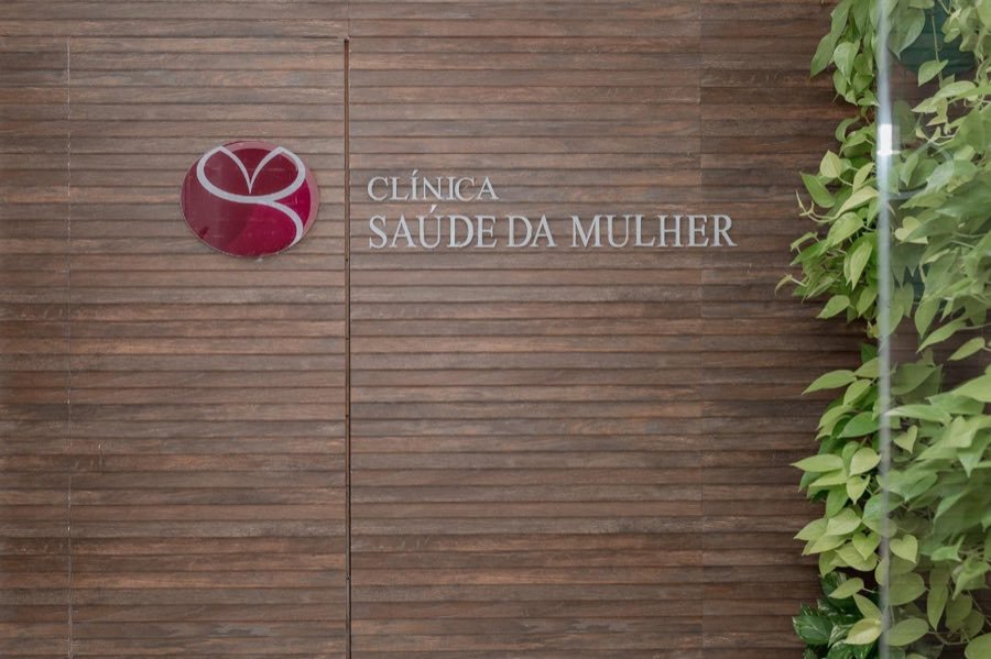 Placa da Clínica Saúde da Mulher na parede de madeira da entrada