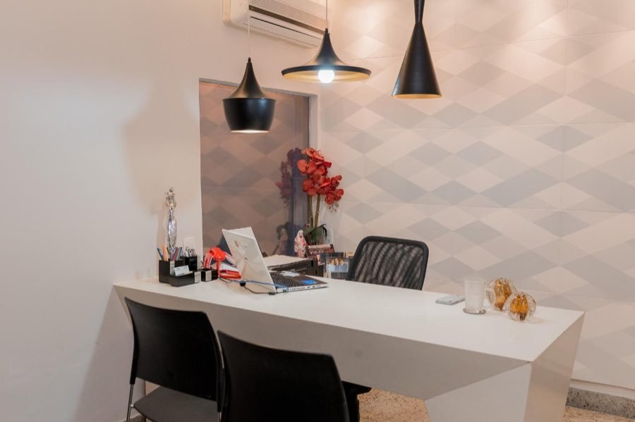 Sala da secretaria, com mesa branca e pendentes pretos